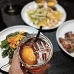 Pink drink with ice and straw over table with plates of food