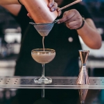 Cocktail in stemmed glass being strained by bartender