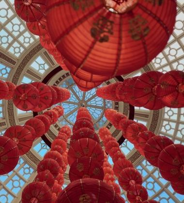 a series of red chinese paper lanterns hang in a glass dome, shot looking up