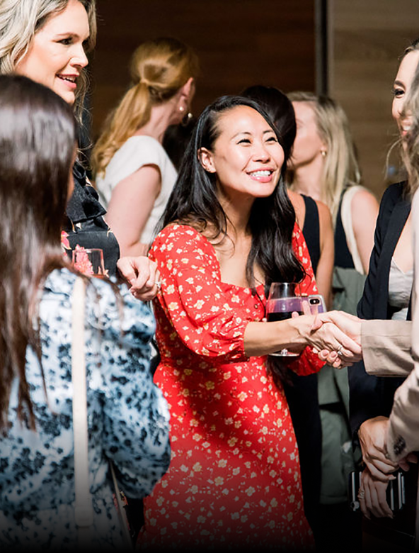 Woman holding wine shaking hands with another woman in a crowd