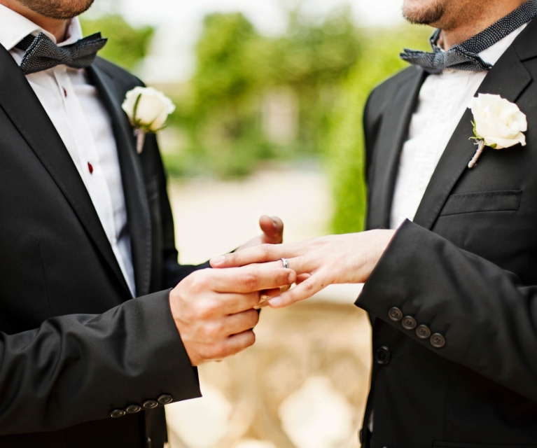 two men exchange wedding bands in suits and bow ties