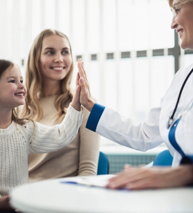 Woman in a medical office with her young daughter giving the doctor a high five.
